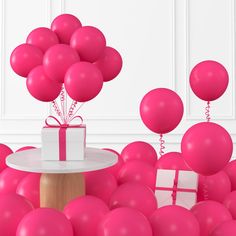 a bunch of pink balloons are in the air near a table with a white present