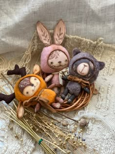 three small stuffed animals sitting in a basket on top of a white cloth covered surface