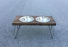 two metal bowls sitting on top of a wooden table in the middle of an empty parking lot