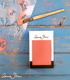 a paint brush sitting on top of a piece of paper next to an orange and pink color swatch