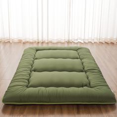 a green futon mattress sitting on top of a wooden floor next to a window