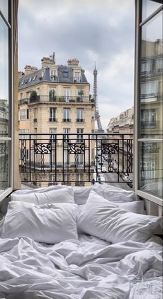 an unmade bed with white sheets and pillows in front of the eiffel tower