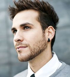 a man with a beard wearing a suit and tie looking off into the distance while standing in front of a building