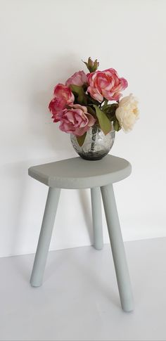 pink and white flowers in a silver vase on a small stool against a white wall