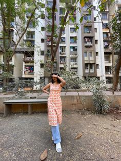 a woman standing in front of an apartment building with her hands on her head and looking up at the sky