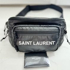 Saint Laurent Nylon Logo Belt Bag/Bumbag (Nwot) Color: Black Argento - Keep Essentials Close To The Body In This Sleek, Sport-Luxe Belt Bag With A Water-Proof Exterior. - Adjustable Belt Strap - Top Zip Closure - Black-Painted Hardware - Three Outside Zip Pockets - Lined Polyester - Made In Italy Size: 16''W X 7''H X 4''D Comes With Original Dust Bag, And Saint Laurent Booklet (Still Has Original Paper Inside (Never Worn - Pre-Loved). Condition Will Be Shown During The Live No Callouts. All Item Travel Nylon Bag With Logo, Luxury Nylon Bag With Zipper Pocket, Luxury Nylon Pouch Bag, Luxury Streetwear Bags With Logo, Luxury Logo Bags For Streetwear, Designer Black Nylon Bag, Black Designer Nylon Bag, Luxury Nylon Bag With Large Capacity, Black Belt Bag Shaped As Shoulder Bag