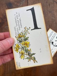 a person holding up a card with the number one on it and flowers in front of them