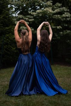 two women in long blue dresses standing on the grass with their hands behind their backs