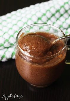 a glass jar filled with brown liquid sitting on top of a wooden table next to a green and white towel