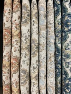 an assortment of rugs hanging up in a row on a rack, with different colors and patterns