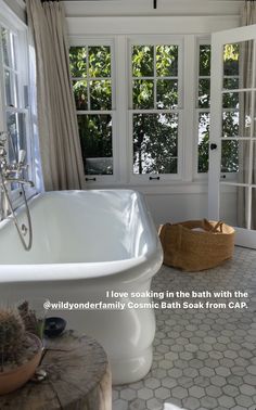 a white bath tub sitting inside of a bathroom next to a wooden stool and window