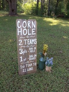 a wooden sign sitting in the middle of a grass covered field next to a tree