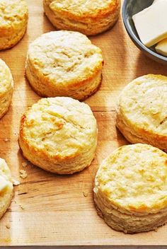 some biscuits and butter are on a wooden board next to a bowl with cheese in it