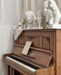 an old piano with statues on top of it in front of a curtained window