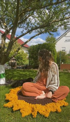 a woman sitting on the ground in front of a tree with yellow flowers around her