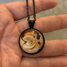 a hand holding a glass pendant with a shell and starfish in it's center