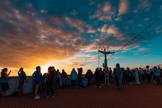 a group of people standing on top of a pier next to the ocean at sunset