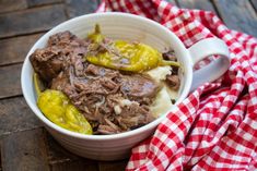 a bowl filled with meat and vegetables on top of a red and white checkered cloth