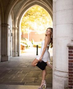 a beautiful young woman posing for a photo in front of an arched archway with her legs crossed