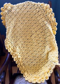 a yellow crocheted blanket sitting on top of a wooden chair