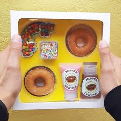 a person holding up a box with doughnuts, candy and other items in it