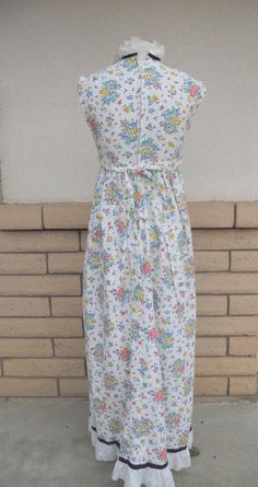 "Vintage 1970's summer dress! Sweetest white eyelet fabric dress with a red, yellow, lavender and green floral and fruit print. Eyelet fabric has small holes edged in machine embroidery. It has an empire waist with attached same fabric belt. The high neckline has a double row of eyelet lace trimmed in black grosgrain ribbon. The bottom is hemmed in a large row of eyelet lace trimmed in matching grosgrain ribbon. Back metal zipper. This adorable dress was custom made. Fabric feels like a cotton/p Casual White Vintage Dress For Garden Party, Vintage White Fitted Sundress, White Fitted Vintage Sundress, White Sleeveless Vintage Dress With Floral Print, Vintage Sundress For Spring Daywear, Vintage Floral Print Sundress For Daywear, Vintage White Sundress For Garden Party, White Vintage Sundress For Garden Party, White Vintage Dress With Floral Print