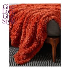 a bed with a red blanket on top of it next to a wooden footstool