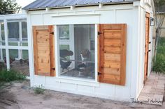 a chicken coop with two chickens in the window and one on the ground looking out