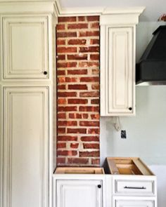 a kitchen with white cabinets and brick wall