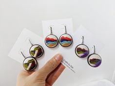 four pairs of earrings with different colors and designs on them are being held up by a person's hand