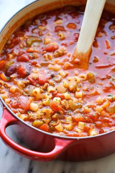 a red pot filled with beans and vegetables on top of a marble counter next to a wooden spoon