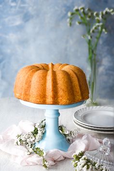 a bundt cake sitting on top of a blue cake stand next to plates and flowers