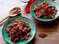 two green plates filled with pecans on top of a wooden table next to spoons