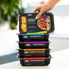 a stack of food containers stacked on top of each other with the lids open and one hand reaching for an entree