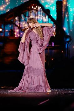 a woman in a purple dress standing on stage with her arms behind her head and hands over her face