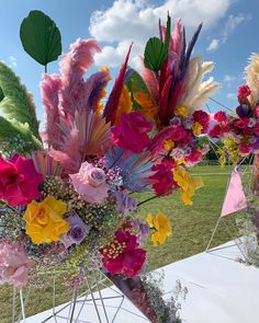 colorful flowers are arranged in vases on a white table cloth covered outdoor area with blue sky and clouds