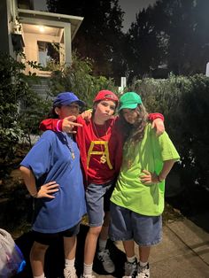 three young children standing next to each other in front of bushes and trees at night