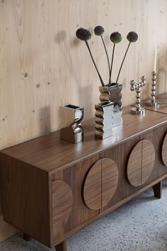 two vases with flowers on top of a wooden cabinet