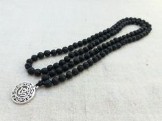 Mala made of 6mm Black Lava beads and OM simbol. This beautiful mala will be a pleasure to recite your mantras with, meditate with, or wear as a beautiful necklace. 108 beads (no knots). It measures approximately 26 inches in total length. Lava Stone is a grounding stone. It gives us strength and courage, allowing us stability through times of change. A calming stone, it is very useful in dissipating anger. Lava Stone enhances fertility. All our jewels arrive carefully packaged in a gift box rea Black 108 Beads Mala For Meditation, Black Mala With 108 Beads For Meditation, Spiritual Black Beads Mala For Meditation, Hand-strung Black Mala For Meditation, Black Hand-strung Mala For Meditation, Spiritual Black Beaded Necklaces For Meditation, Spiritual Black Beaded Necklaces, Black Spiritual Mala For Healing, Silver Mala With 108 Beads For Meditation