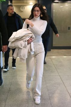 a woman in white is walking through an airport with her jacket open and looking at the camera