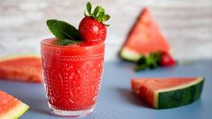 a glass filled with watermelon and strawberries on top of a blue table