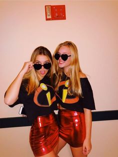 two young women wearing black sunglasses and shiny red shorts, both with their arms around each other's shoulders