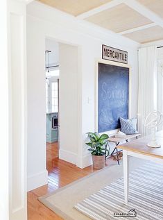 a living room with white walls and wood flooring on the wooden floor, along with a chalkboard in the corner