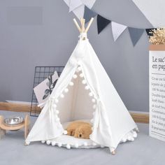 a small teepee tent with pom poms on the front and sides, next to a sign that says le sace en papillon