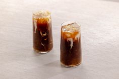 two glasses filled with iced coffee sitting on top of a white table next to each other