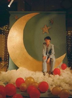 a man sitting on top of a moon surrounded by red and gold balloons in front of a backdrop