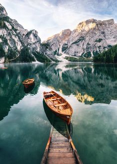 two boats docked at the end of a pier in front of mountains and water stock photo