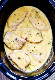 a crock pot filled with chicken and gravy on top of a wooden table