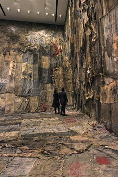 two people standing in front of a large rock wall