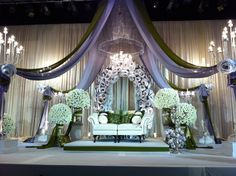 a stage set up for a wedding with white and green decorations on the sidelines